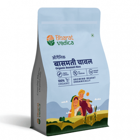 A light blue and white packet of Bharat Vedica brand Organic Basmati Rice, with text in both Hindi and English. The packet features the brand logo at the top and an illustration of a farmer and a woman in a field of rice at the bottom. The text on the packet reads "ऑर्गेनिक बासमती चावल Organic Basmati Rice" and "100% ORGANIC GROWING BHARAT ORGANICALLY".